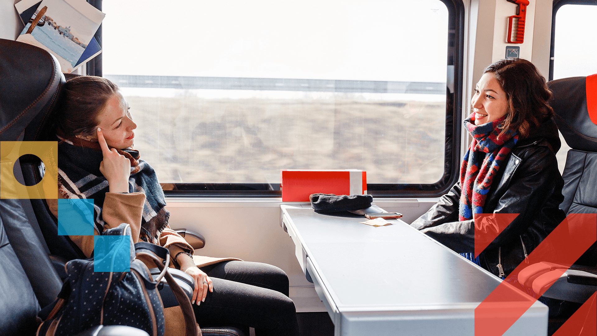 Two young women sitting across from each other in a train booth, talking and smiling.