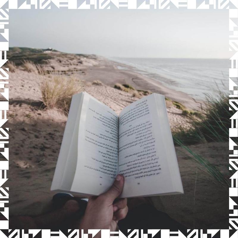 A person holding a book while sitting at the beach