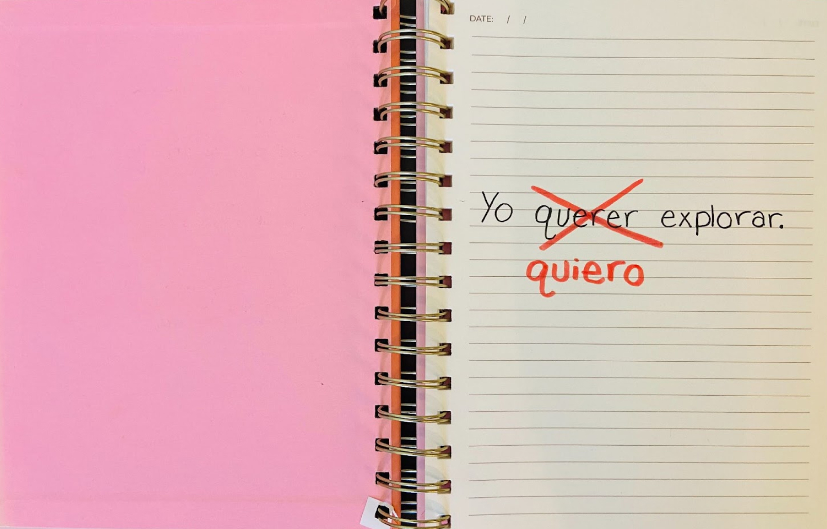 An open notebook where someone has written "Yo querer explorar" and has crossed out "querer" to replace it with "quiero"