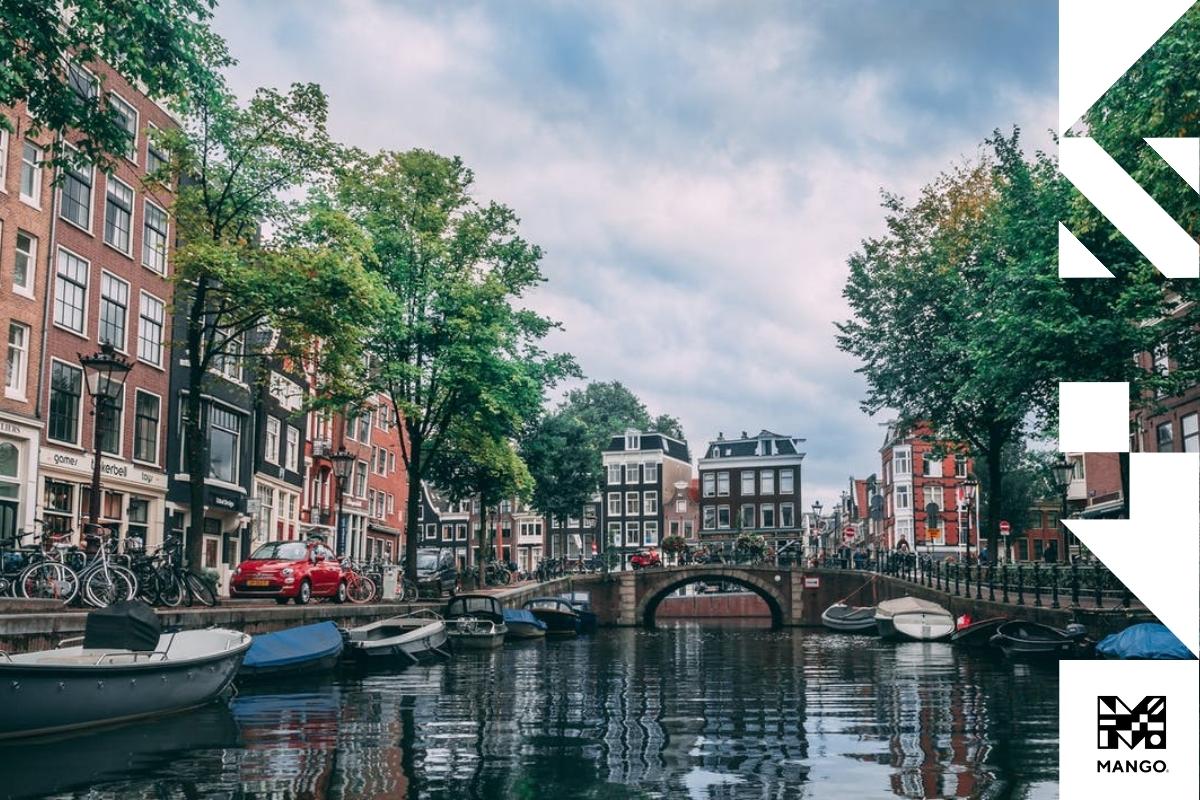 A city shot of a Dutch city divided by a channel surrounded by cars, bikes and buildings