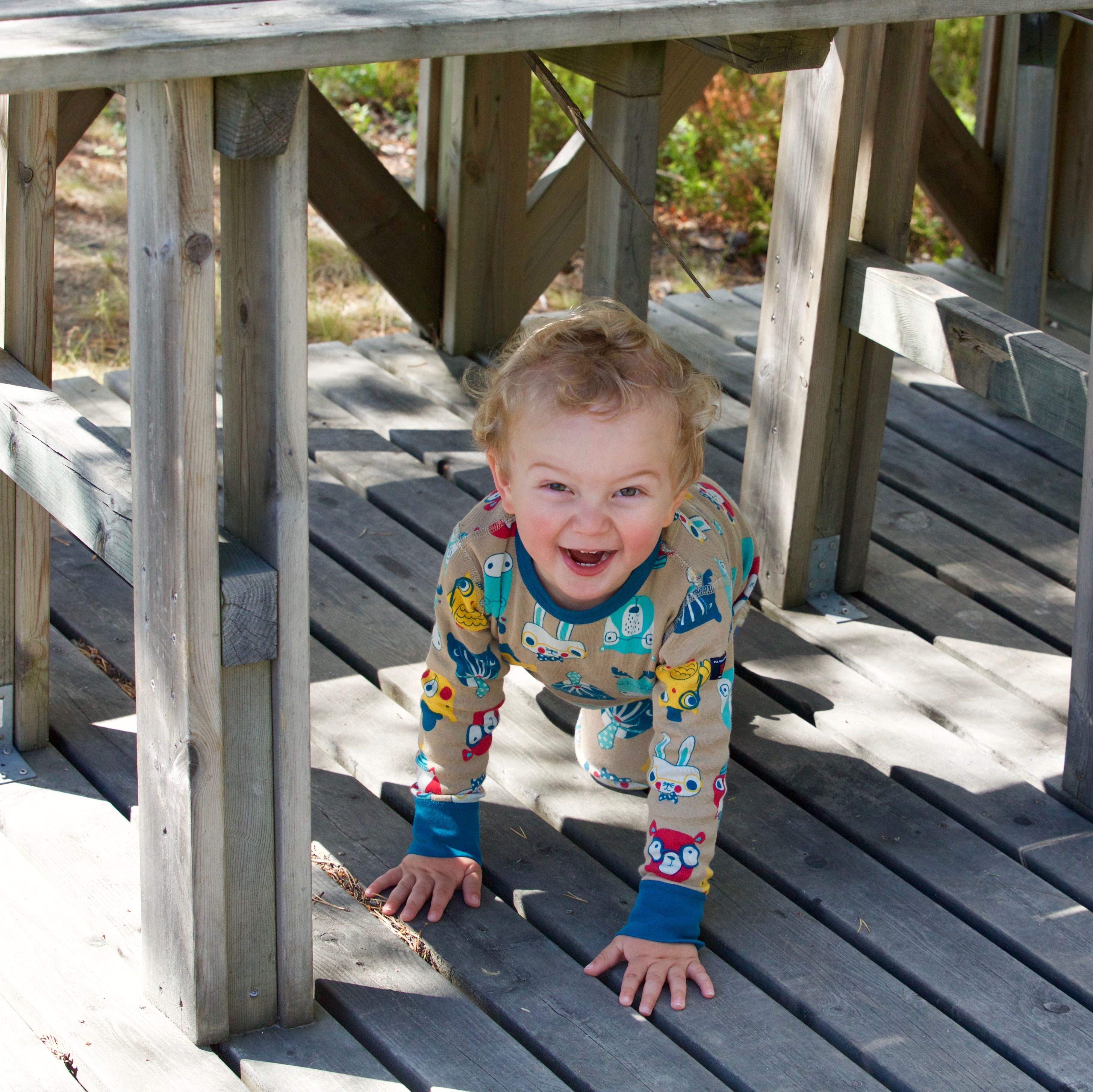 A young child in pajamas with curly hair smiles from under an outdoor table