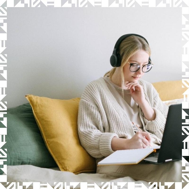 A young girl sitting on a couch wearing a pair of headphones and writing on a notebook.