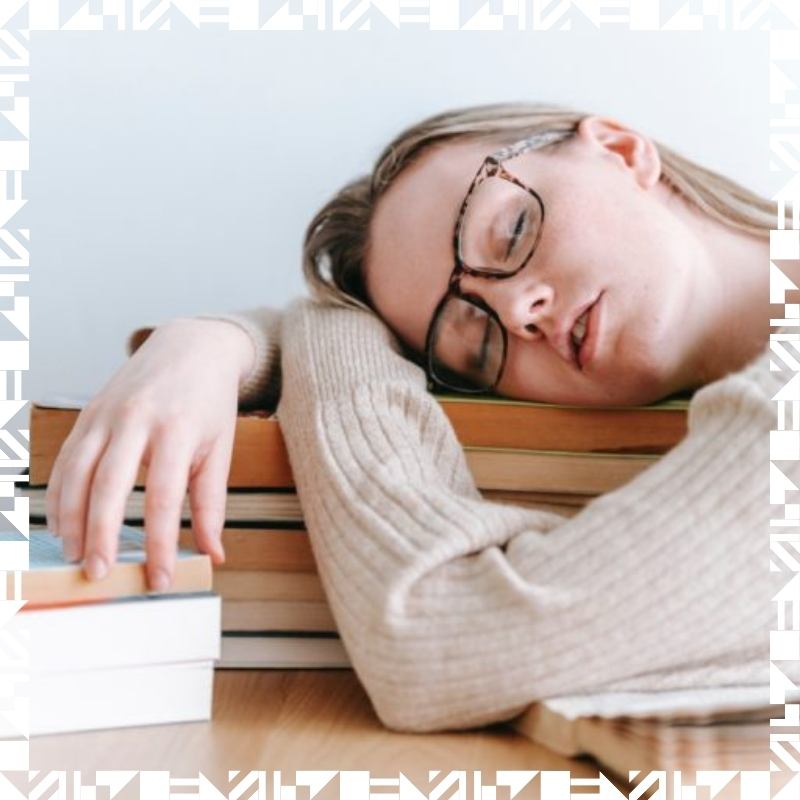 A young girl wearing glasses sleeping on a pile of books on her desk