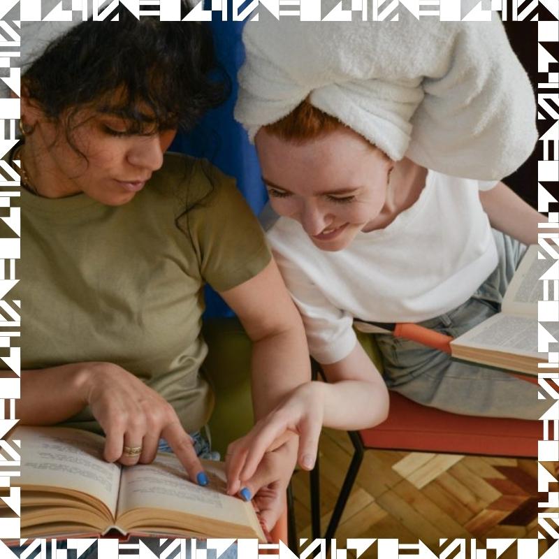 Two young women with their hair wrapped in towels reading books together