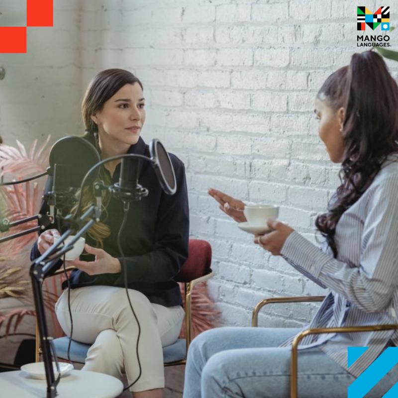 Two young women talking in front of two microphones while sipping on coffee