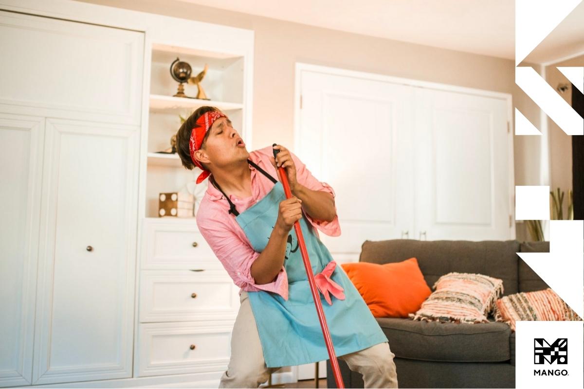 A young man with a broom and cleaning gloves cleaning an apartment