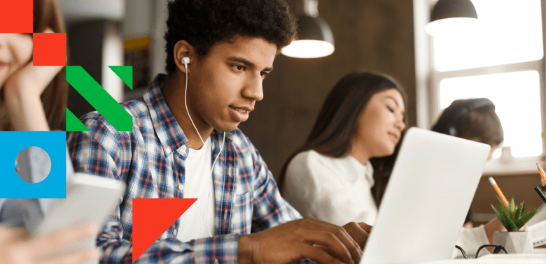 A young man in a library/study hall wearing headphones working on his laptop